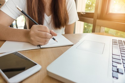 Mädchen schreibt etwas auf Papier vor einem Laptop